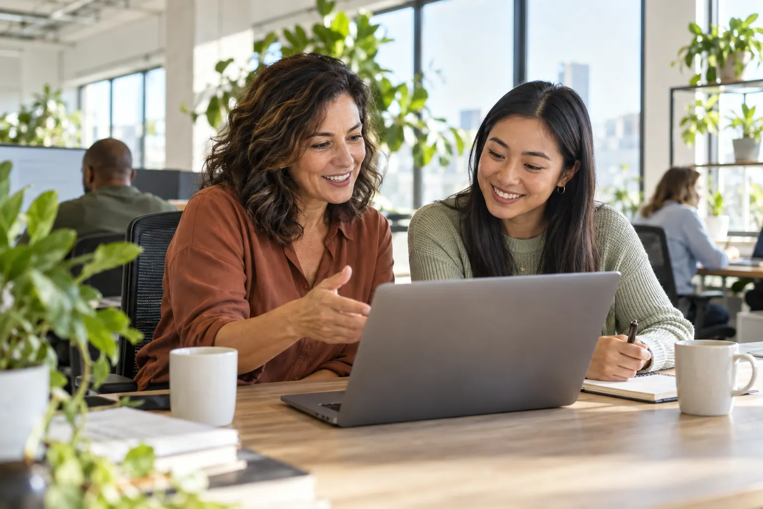 A manager and an employee smile while reviewing a plan together on a laptop in a bright office