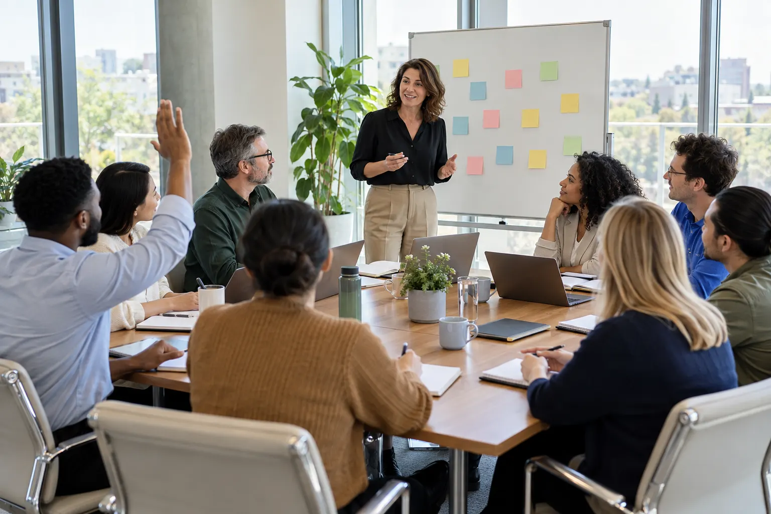 A facilitator stands by a whiteboard of sticky notes while an employee at the meeting table raises his hand