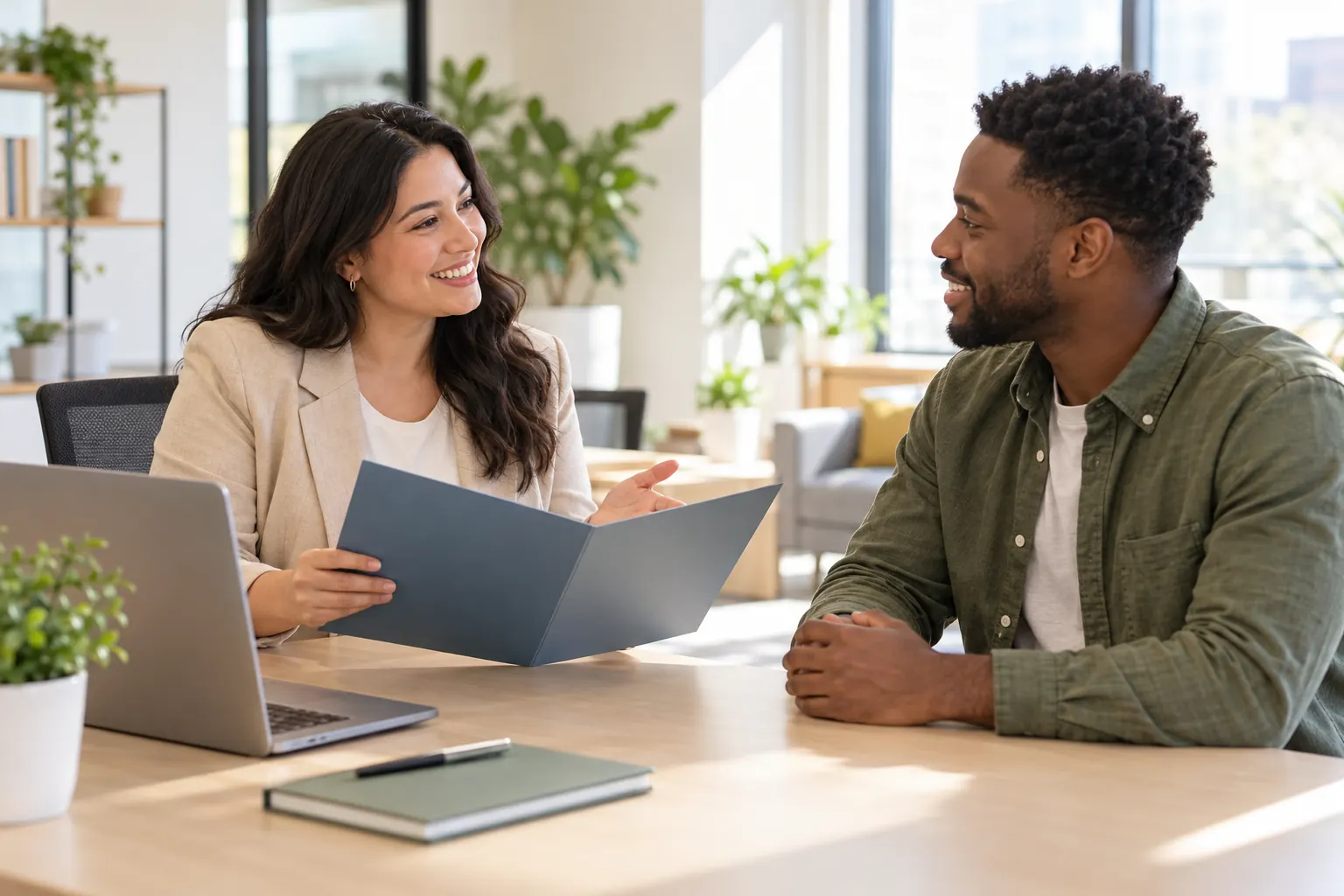 A smiling HR specialist opens a welcome folder for a new hire across a desk in a sunny office.