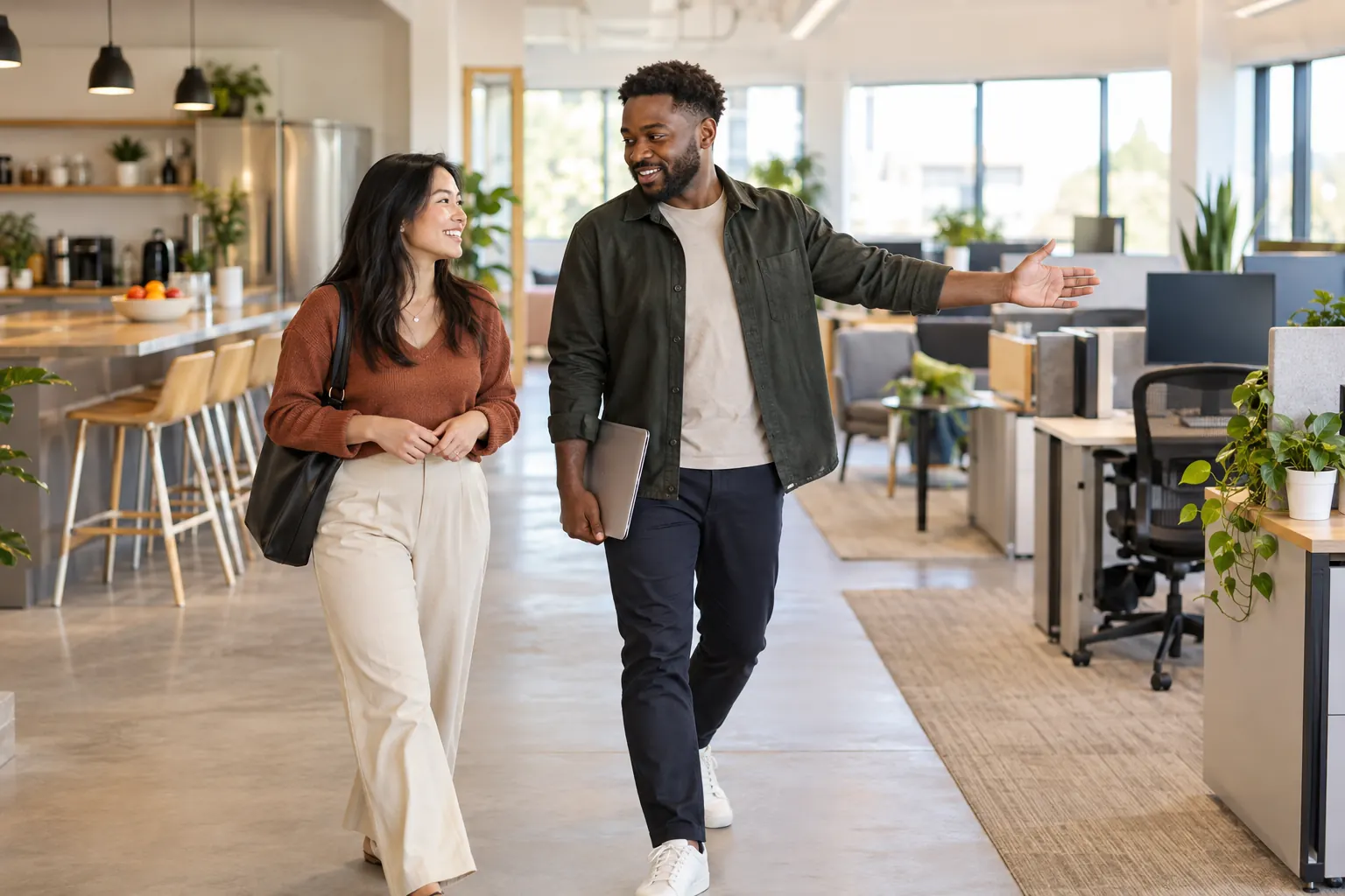 A coworker points out the open-plan office to a new colleague as they walk past the kitchen.