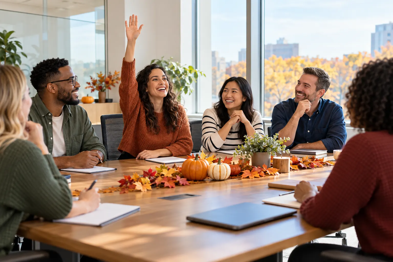 Coworkers around a conference table set with autumn leaves and small pumpkins, one raising her hand to answer.